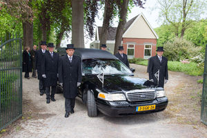 Rouwauto, dragers en nabestaanden verlaten het terrein van aula Memory